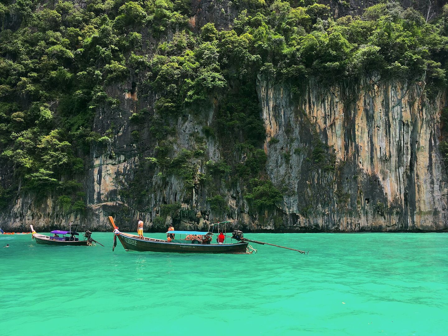 Long-tail boats on emerald water beneath limestone cliffs in Pileh Lagoon, Phi Phi Leh